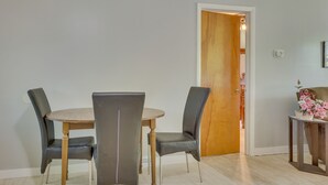 Ein Essbereich mit einem runden Tisch, vier Stühlen, einer Holztür und einem kleinen Tisch mit Korb und Blumen.