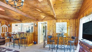 L’intérieur d’un chalet en bois comprend un coin bar avec des tabourets, un téléviseur et une cheminée.