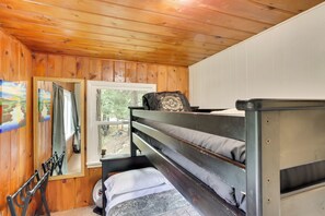 Una camera in una baita di legno con letti a castello, una finestra e uno specchio.