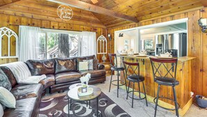 L’intérieur d’un chalet en bois, avec un canapé en cuir, un coin repas doté de tabourets de bar et une cuisine visible à travers une porte ouverte.