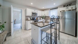 A modern kitchen with white cabinets, a stainless steel refrigerator, and a central island with bar stools.