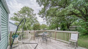 A wooden deck with a round table and chairs, a hanging chair, and a sign with a message.