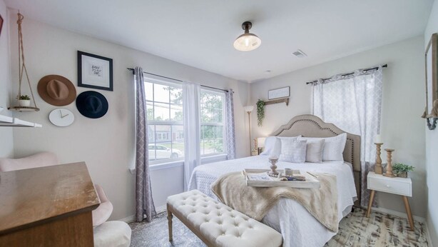 A bedroom with a bed, bedside table, bench, and a window with curtains.