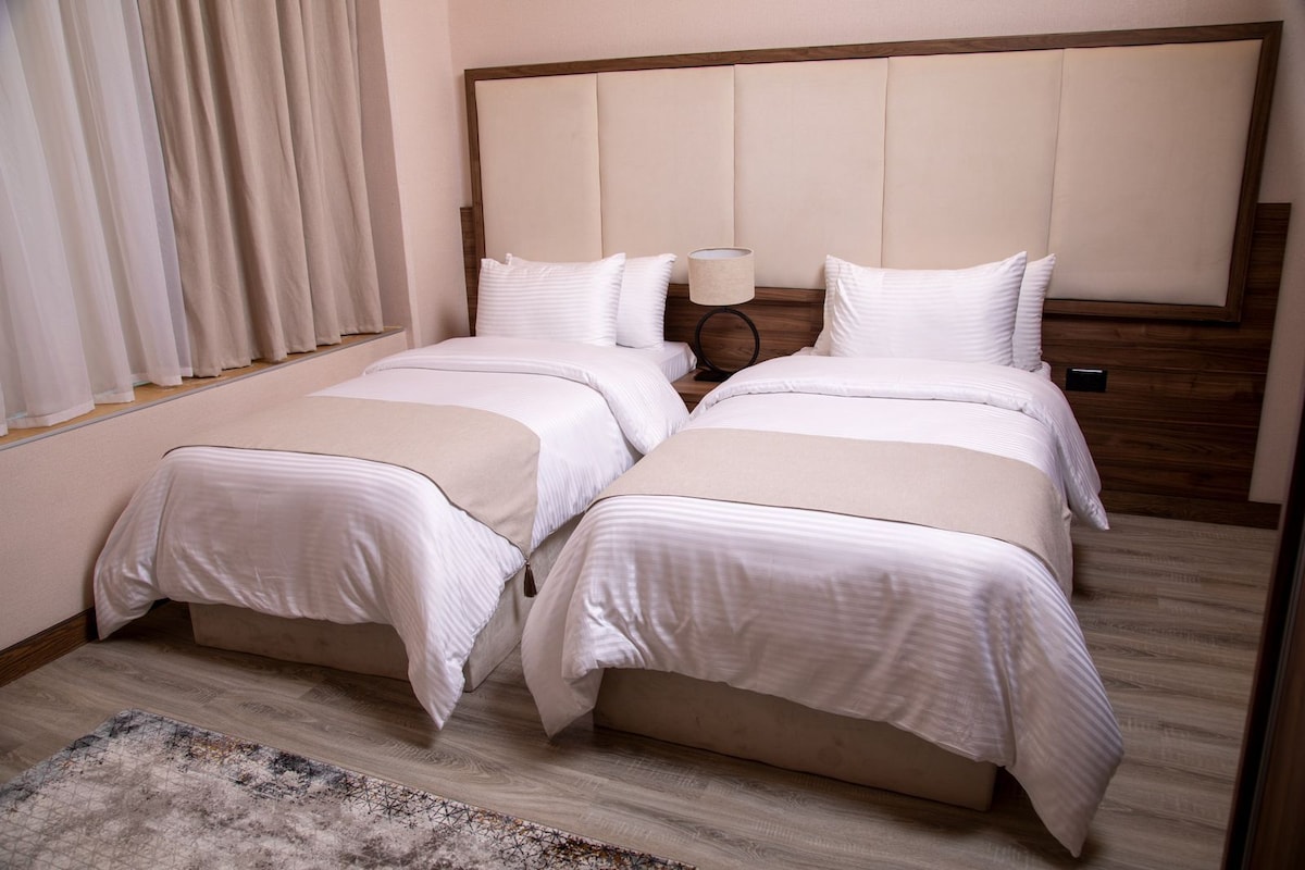 A double bed with a wooden headboard, a bedside table with a lamp, and a patterned rug on a wooden floor.
