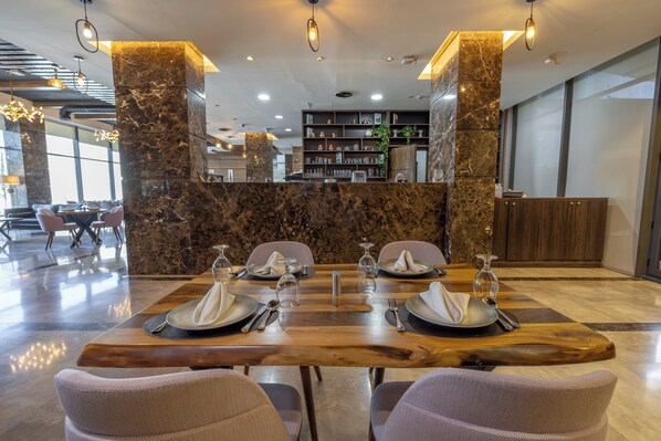 Un restaurante con mostrador de recepción de mármol, mesa de comedor de madera y sillas modernas.