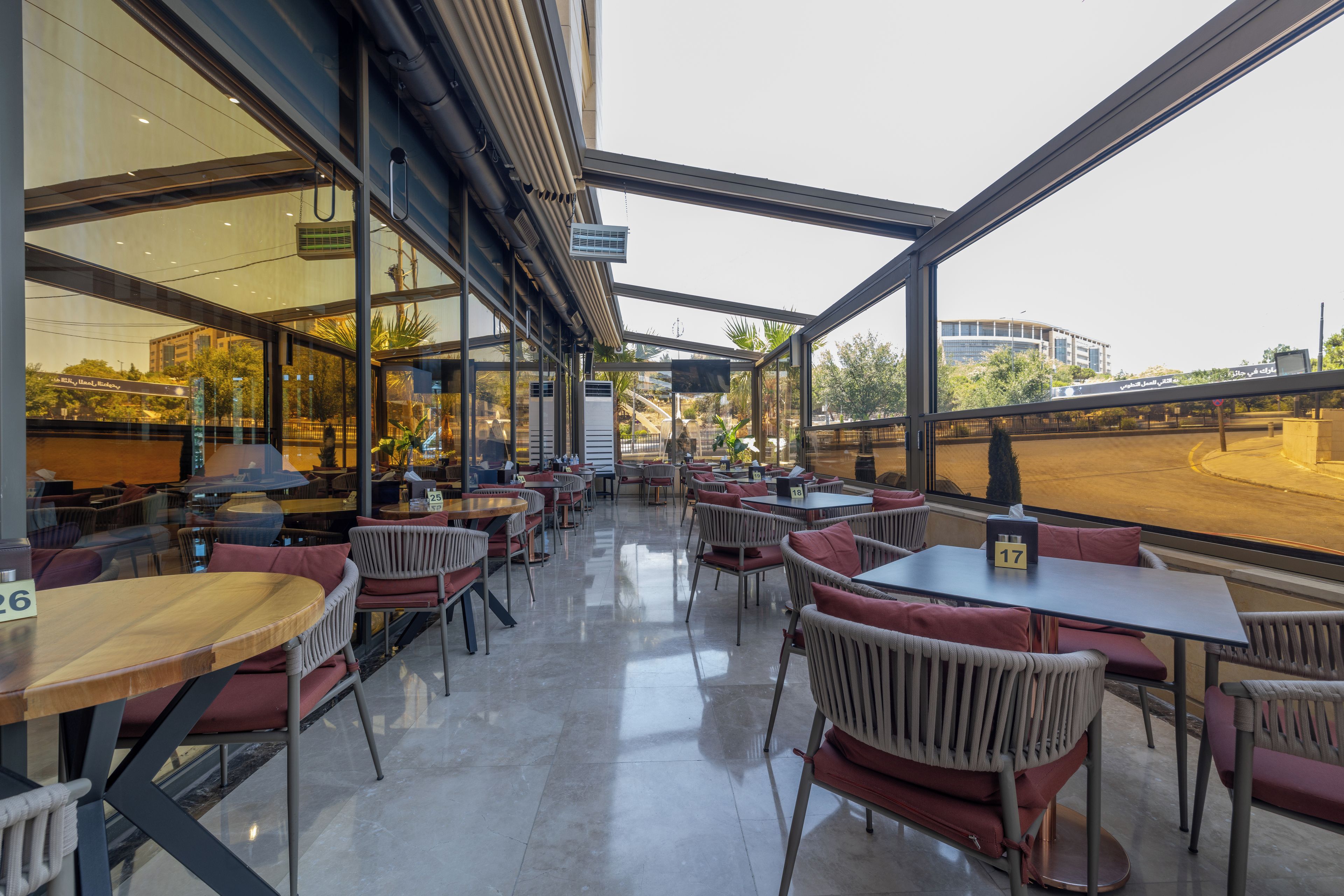 Un café con espacio interior y exterior, paredes de vidrio, mesas y sillas.