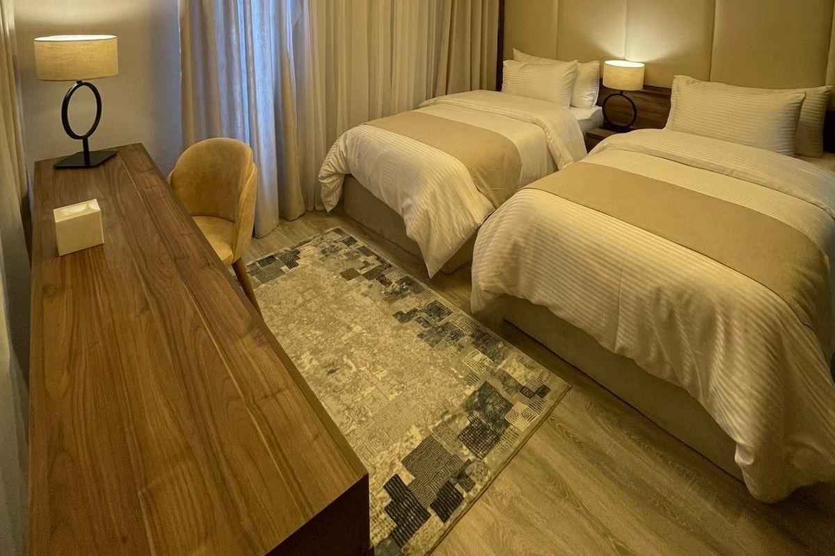 Una habitación de hotel con dos camas, un escritorio, una silla y una lámpara en el techo.