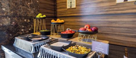 A buffet with various fruits and salads, a marble wall, and wooden paneling.