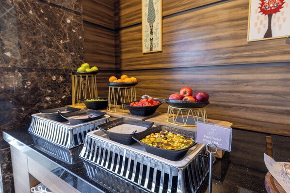 A buffet with various fruits and salads, a marble wall, and wooden paneling. - Jeddah Homes Boutique Hotel (Amman)