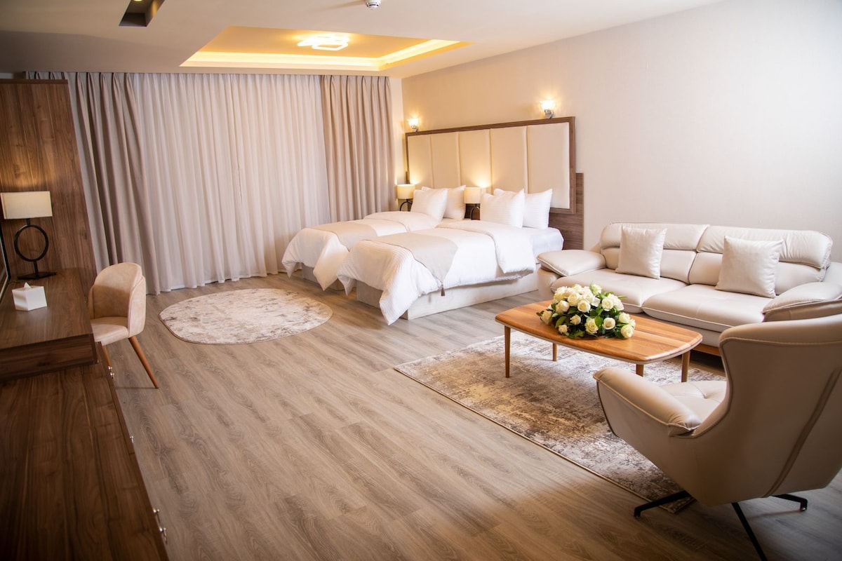 Habitación de hotel con cama, sofá, mesa de centro con flores, escritorio y una silla.