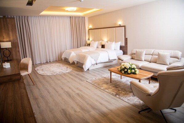 A hotel room with a bed, a sofa, a coffee table with flowers, a desk, and a chair. - Jeddah Homes Boutique Hotel (Amman)