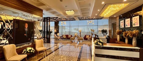 A spacious lobby with a modern design, featuring a large seating area, a reception desk, and a view of the city through large windows.