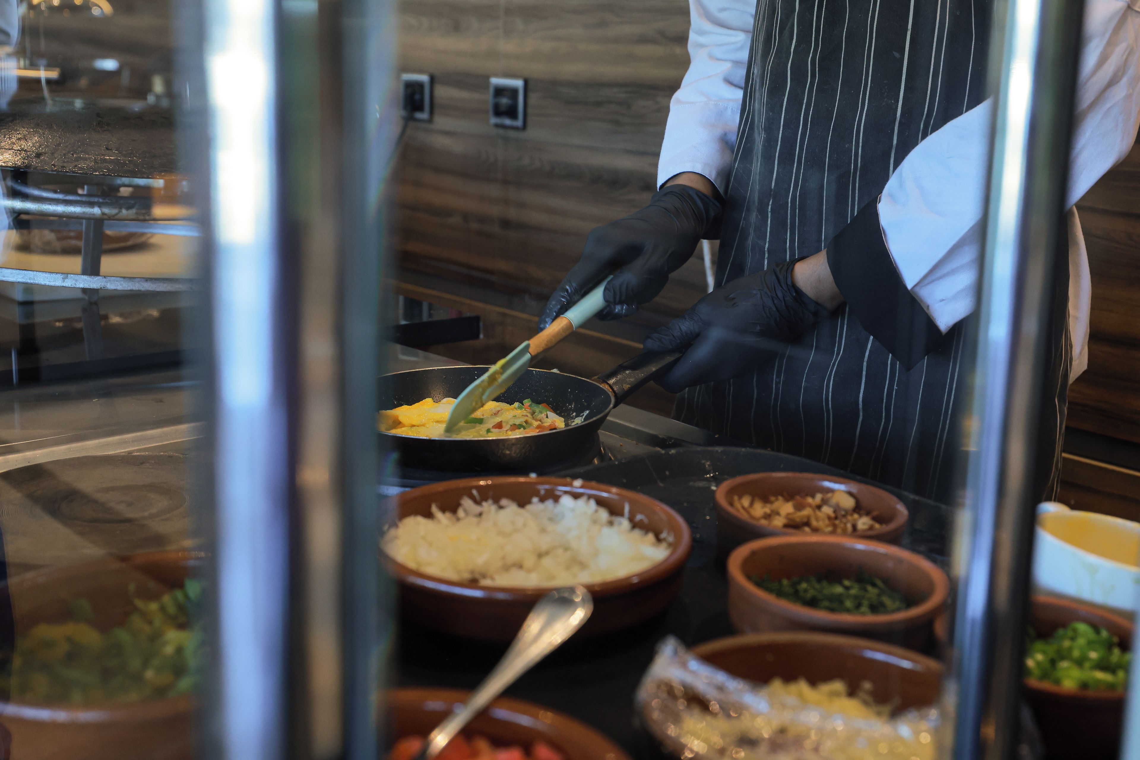 A person cooking in a kitchen with various bowls of ingredients and a frying pan on a stove.