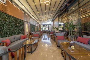 A modern indoor seating area with tables and sofas, a green wall, and a view through large windows. - Jeddah Homes Boutique Hotel (Amman)