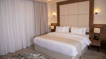 A hotel room with a large bed, two bedside tables, a headboard, and a window with curtains.