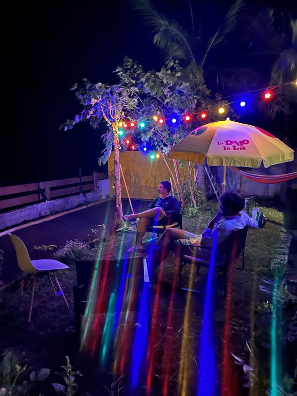 Two people sitting under a tree with colorful lights and a yellow umbrella. - Dodo House (Saint-Leu)