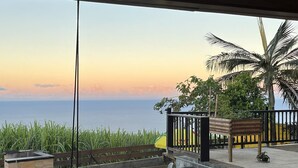 Zona de piscina con vista al mar al atardecer, una terraza de madera y un banco.