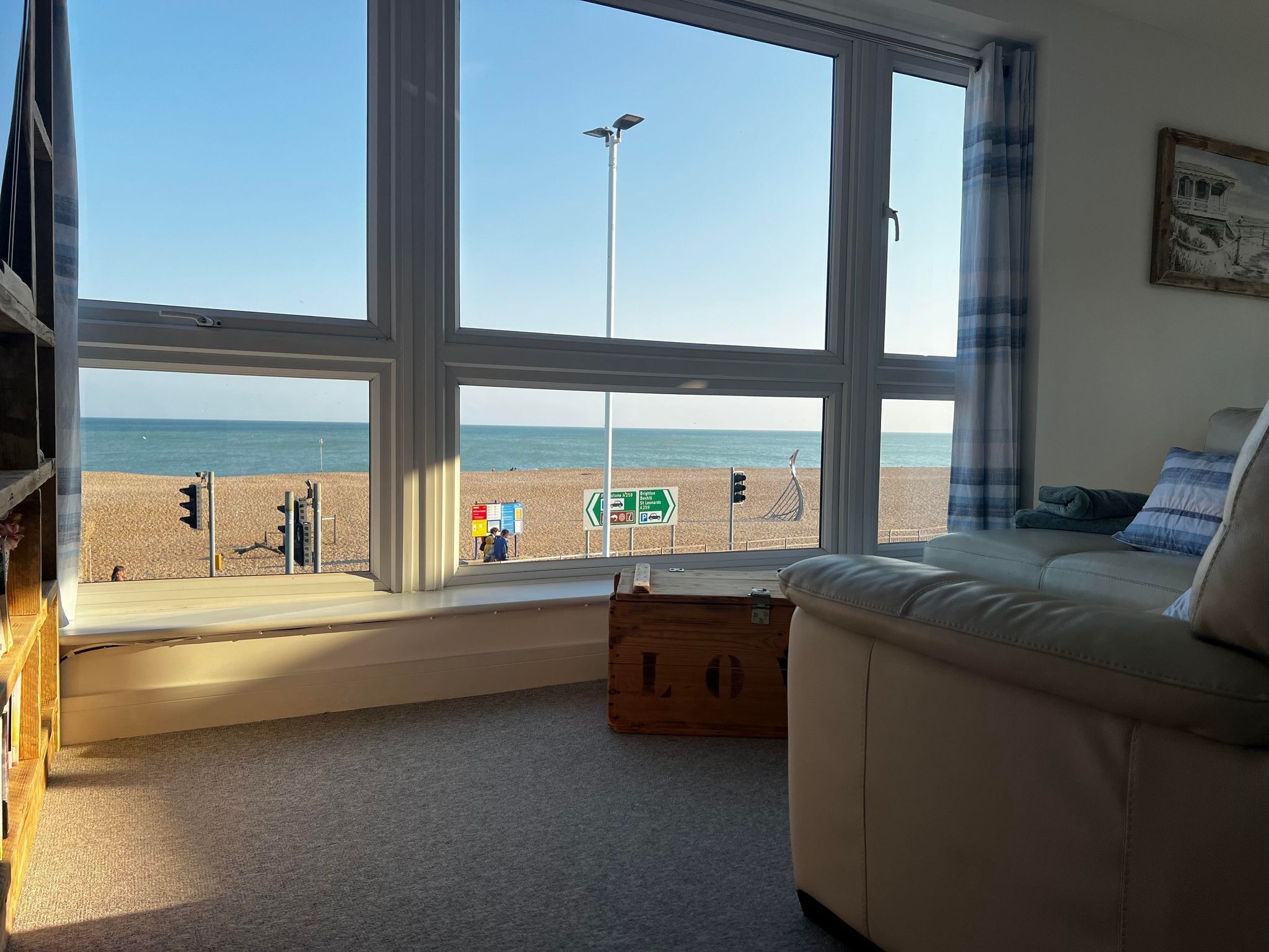 Una habitación con un amplio ventanal con vistas a una playa, un sofá y un baúl de madera.