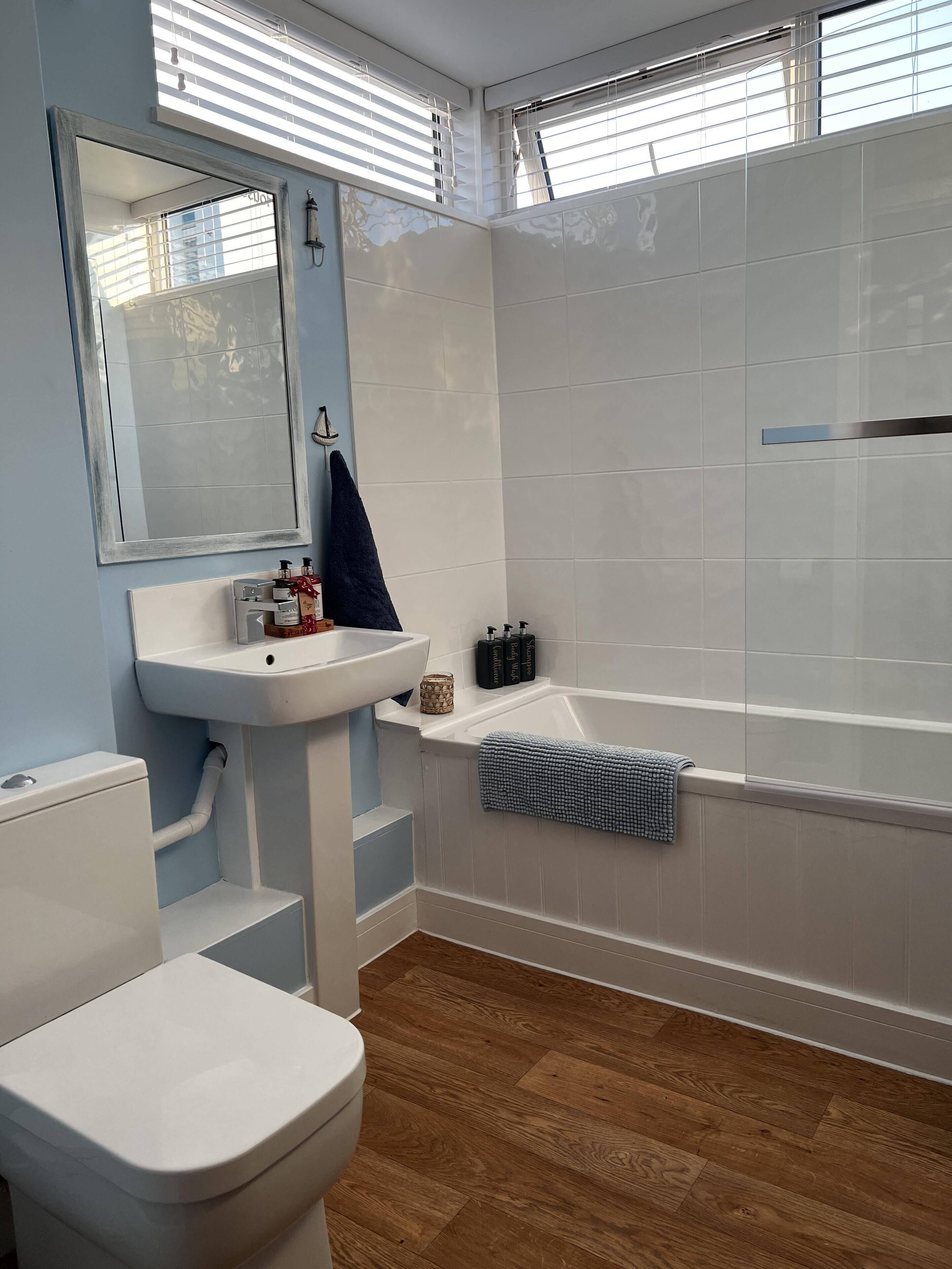 Ein Badezimmer mit Waschbecken, Toilette und Badewanne. Auf dem Waschbecken stehen Flaschen und ein Handtuch hängt an der Badewanne.