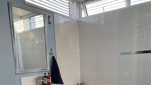 Une salle de bain avec un lavabo, des toilettes et une baignoire, tous de couleur blanche. On peut voir des bouteilles sur le lavabo et une serviette accrochée à la baignoire.