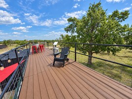 Een houten terras met een metalen hekwerk, een tafel met stoelen en een boom op de achtergrond.