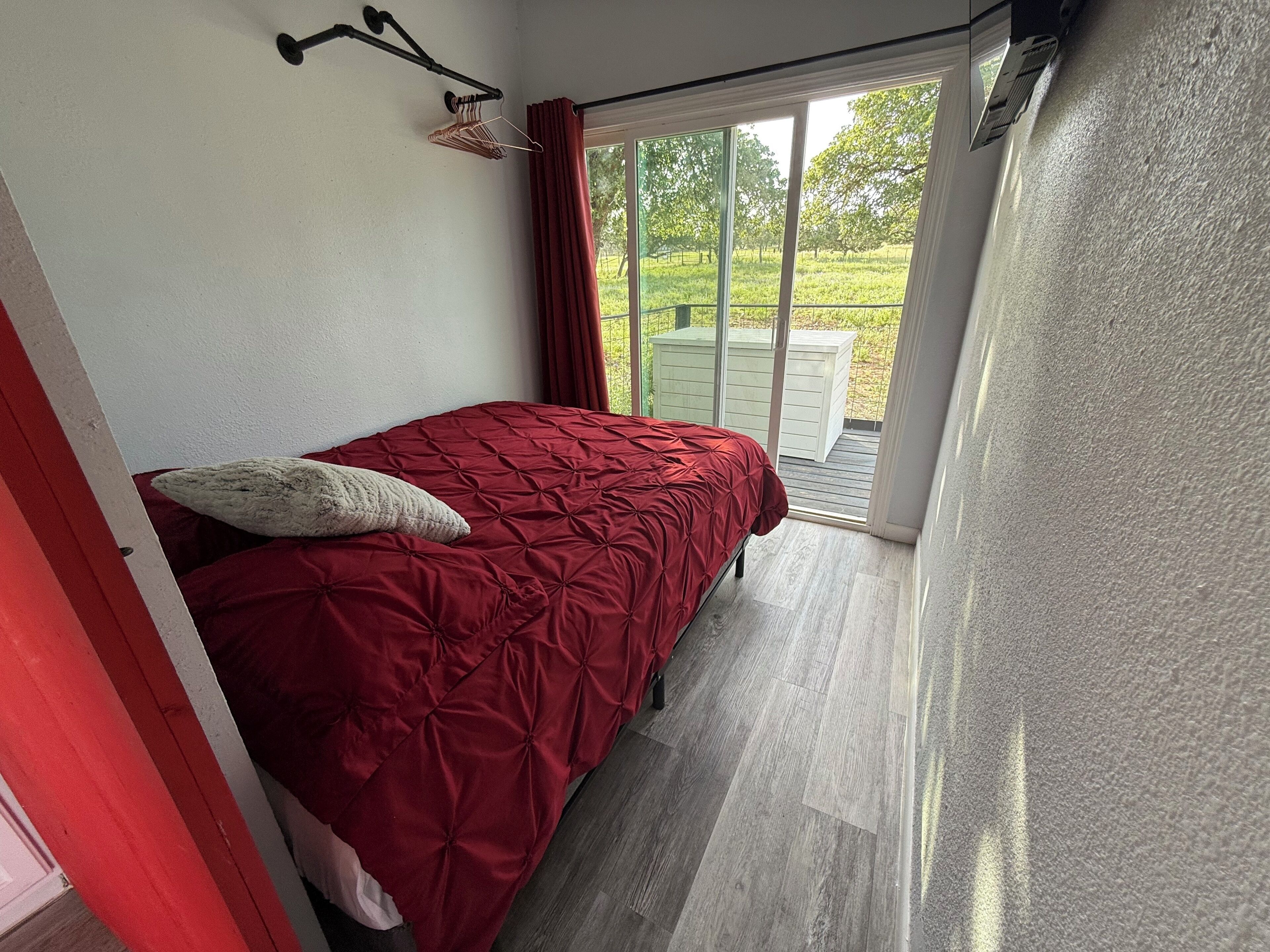 A bedroom with a bed, a hanging light fixture, and a view of a garden through a sliding door.