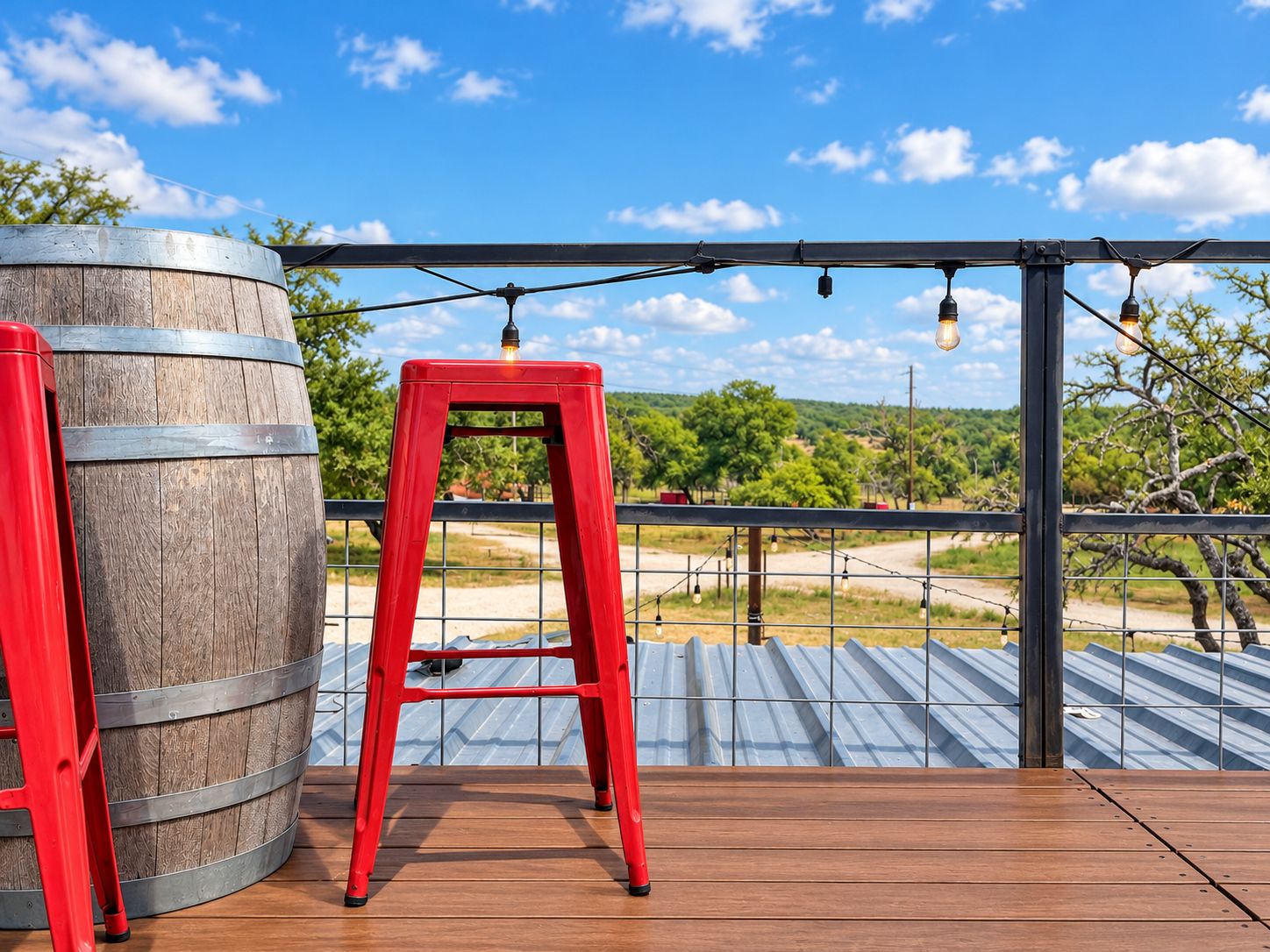 A wooden deck with a red stool and a barrel, overlooking a landscape with trees and a clear sky.