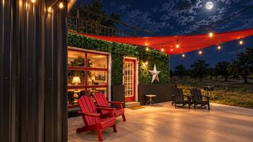 An outdoor patio area with red Adirondack chairs, a barbecue grill, and string lights.