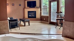 A room with a fireplace, a television, a seating area, and a window with blinds. - Abbey Chateau Treehouse #10 / Oak Crest (Eureka Springs)