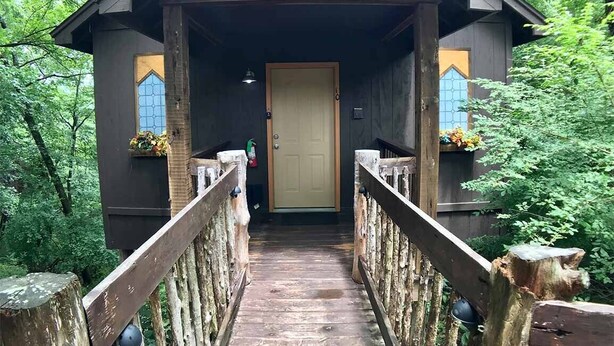 A wooden covered bridge leading to a rustic building with a door and windows. - Abbey Chateau Treehouse #10 / Oak Crest (Eureka Springs)