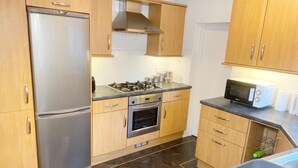 A modern kitchen with a stainless steel refrigerator, a gas stove, an oven, wooden cabinets, and a microwave.
