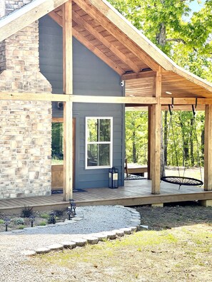 Une maison moderne avec une façade en pierre, une terrasse en bois et un fauteuil suspendu.