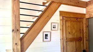 Una escalera de madera con barandal metálico, una pared blanca con paneles horizontales y una puerta de madera.