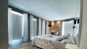 A bedroom with a large bed, a stone accent wall, a wooden floor, and a sliding glass door leading to a balcony. - Pensión Casa Sampedro (Muros)