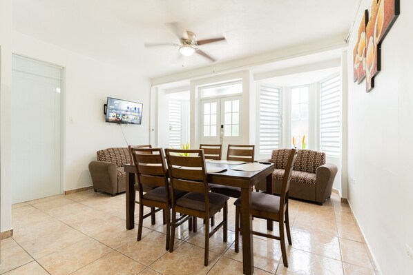 A dining area with a table and chairs, a ceiling fan, and a TV mounted on the wall. - Family Vacation with an Amazing Pool (Aguada)