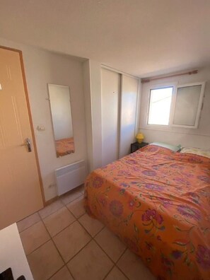 A bedroom with a bed, a wardrobe, a radiator, a window, and a nightstand with a lamp.