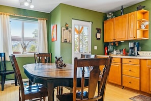 Uma área de refeições com uma mesa redonda e cadeiras, uma cozinha com armários de madeira e uma janela com cortinas.