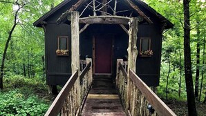 Une cabane rustique avec un escalier en bois menant à une porte rouge, le tout entouré d’une forêt dense.