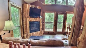 Un salon chaleureux avec une cheminée, un téléviseur et une grande fenêtre donnant sur une terrasse.