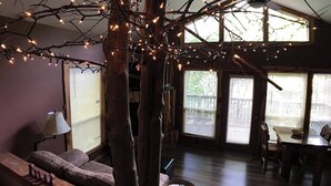 Un salon chaleureux avec un grand arbre décoré de guirlandes lumineuses, un canapé, une table et une lampe.