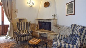 Ein Zimmer mit Kamin, gemusterten Sesseln, einem Schachbrett und einer Wanduhr.