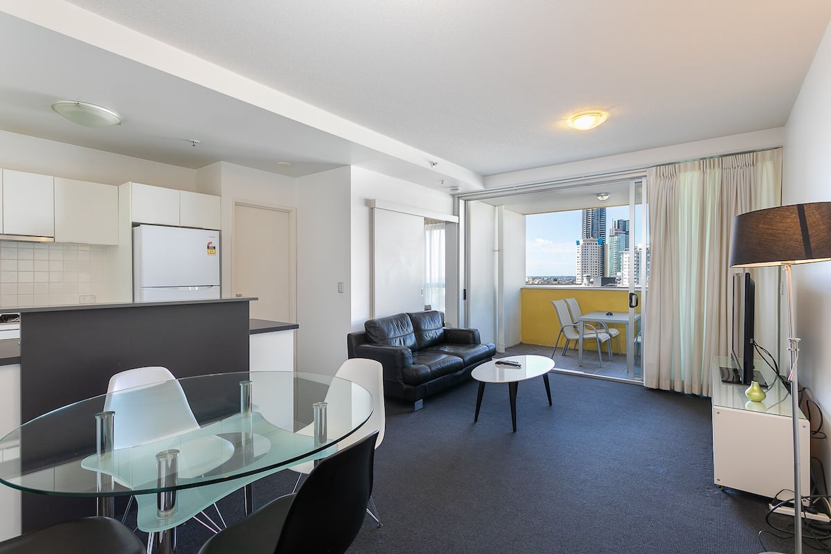 Una habitación de hotel moderna con una mesa de comedor de vidrio, un sofá de cuero negro y una pequeña mesa redonda.