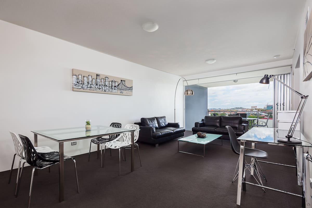Una sala de estar moderna con una mesa de comedor de vidrio, un sofá de cuero negro y vistas a la ciudad a través de amplios ventanales.