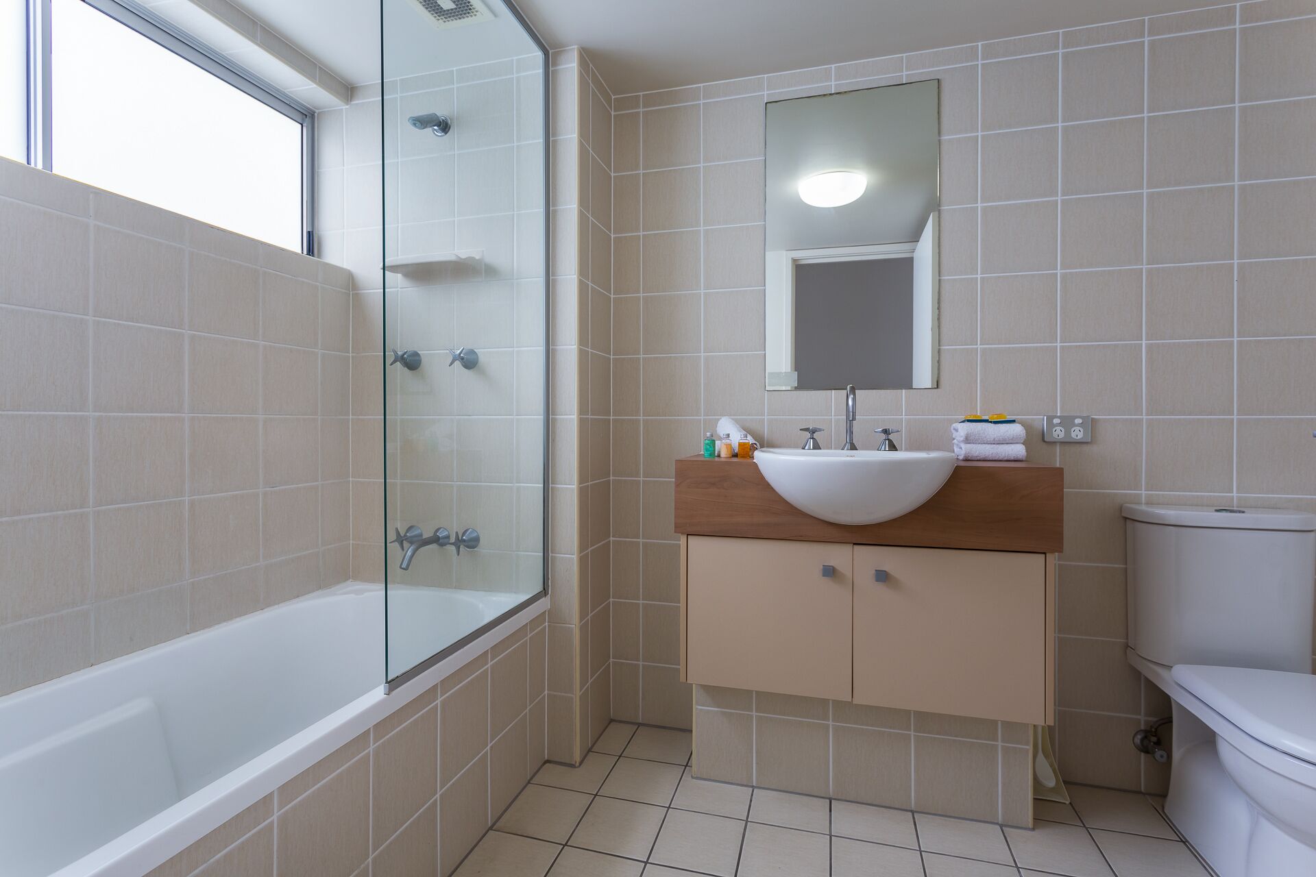 Un bagno moderno con cabina doccia in vetro, una vasca da bagno bianca, un mobile bagno in legno con lavandino e il water.