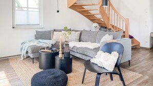 A modern living room with a grey sofa, black coffee table, and a wooden staircase.