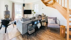 A modern living room with a grey sofa, a black coffee table, a wooden staircase, and a fireplace.