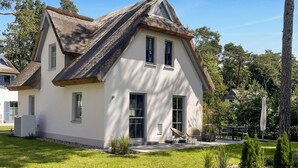 A house with a thatched roof and white walls, surrounded by a well-maintained lawn and trees.
