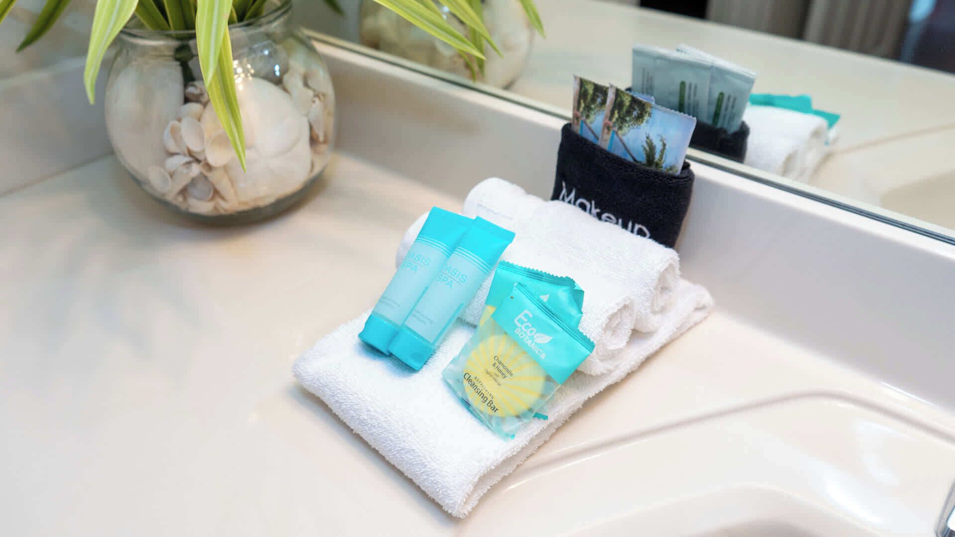 Un lavabo de salle de bain avec une serviette blanche, un bocal en verre contenant des boules de coton et un récipient noir contenant des cartes.