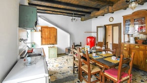 Una cocina rústica con una mesa de comedor dispuesta para cuatro, sillas de madera, un refrigerador rojo y un reloj en la pared.