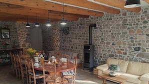 Un interior rústico con pared de piedra, vigas de madera en el techo, una mesa redonda de madera para comer y un sofá.